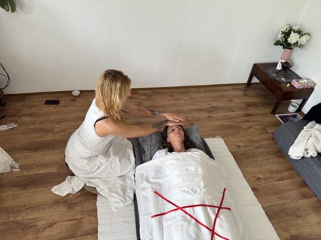Schoßraum-Harmonisierung: Monika legt einer liegenden Frau die Hände auf