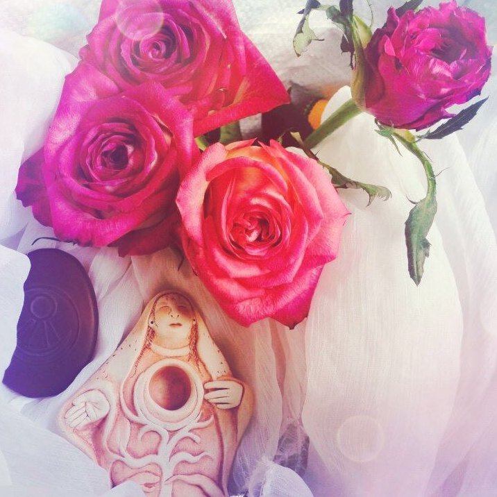 Rosen auf weißem Tuch mit einer Göttinnen-Figur und Mondsymbol